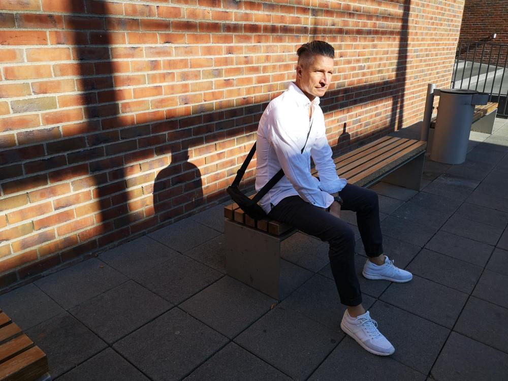 muskarac sa belom kosuljom i patikama sedi na klupi