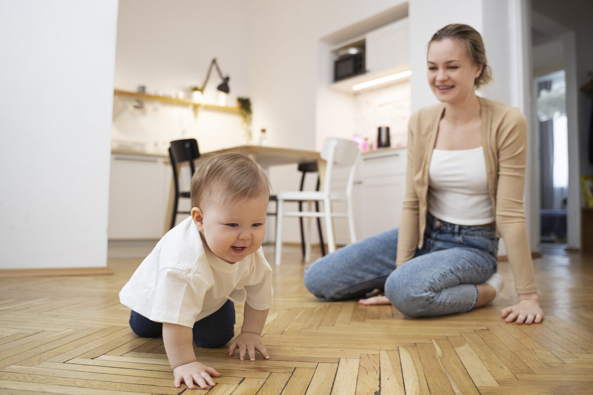 Mama sedi na podu dok beba pokusava da puzi pored nje